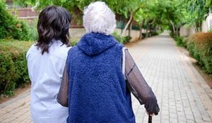 In-Home Senior Caregiver Providing Companionship And Helping Elderly Woman To Go For A Walk Outside. 