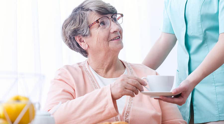 In-Home Dementia Care Provider Serving Tea To A Senior Citizen